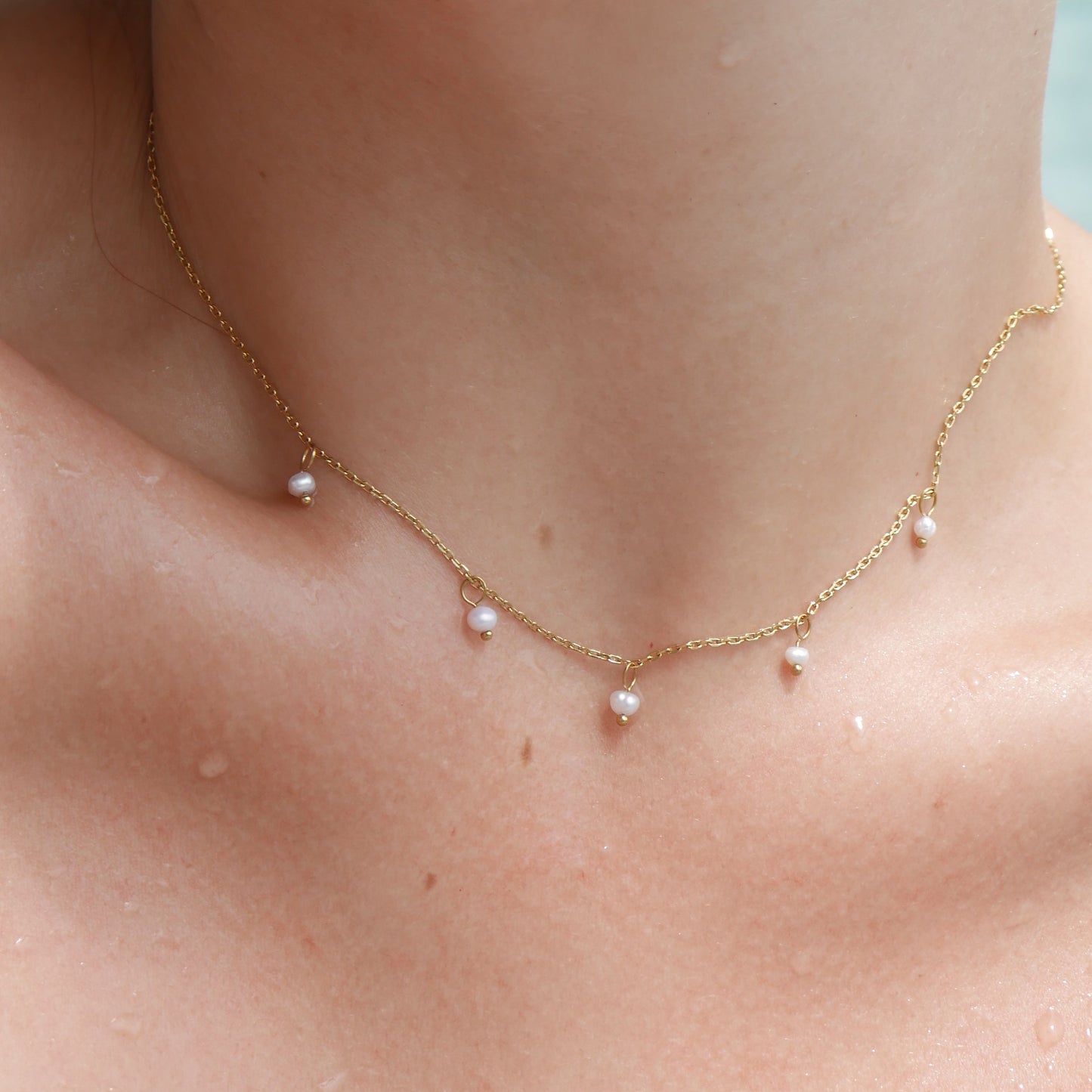 Close-up of a gold necklace with small pearls worn by a person.