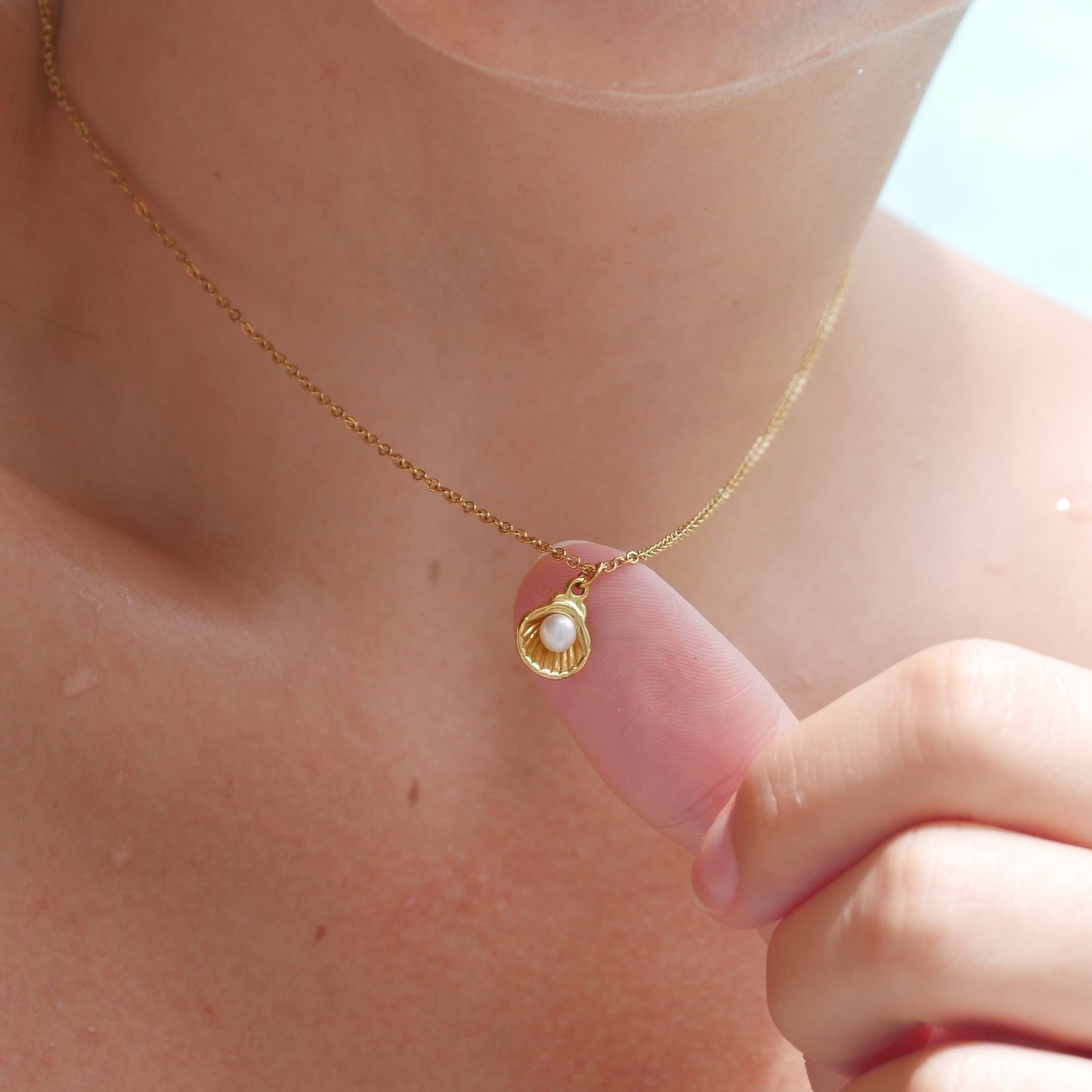 Gold shell necklace with a pearl pendant worn by a person